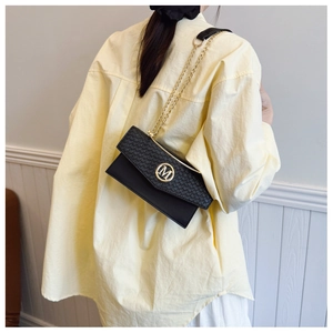 Detail of black woven texture leather bag with gold M logo and chain strap on shoulder