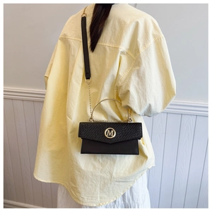 Detail of black woven texture crossbody bag featuring a golden M logo and metal ring handle