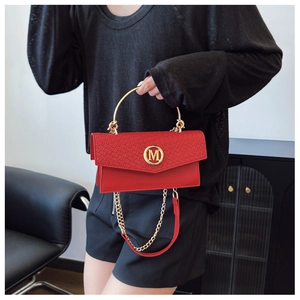 Detail of red croc-embossed crossbody bag with golden metal handle and M logo charm
