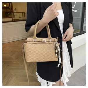 Detail of khaki tote bag featuring checkered embossing and a silk scarf chain accessory