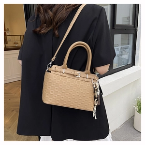 Detail view of khaki embossed tote bag with decorative chain and detachable strap on model