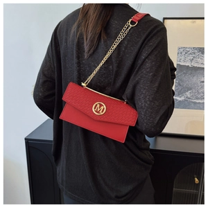 Detail of red crossbody bag featuring woven texture flap and gold M metal emblem logo