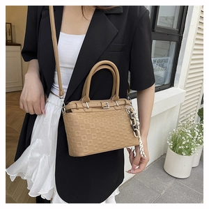Detail of khaki leather tote with checkered texture and woven charm on a street model