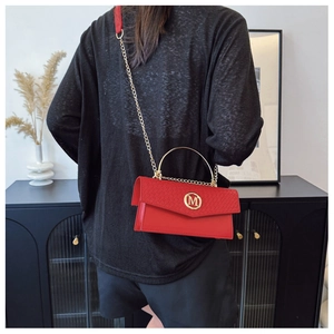 Detail of red leather bag showing crocodile pattern flap and golden metal M logo