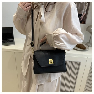 Detail of black lychee grain leather crossbody bag with golden twist lock on a white desk