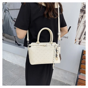 Detail of cream crossbody bag with textured grid pattern and scarf charm on long strap