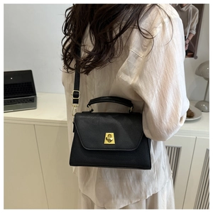 Detail of black lychee grain leather crossbody bag with golden rectangular turn-lock