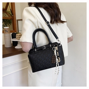 Detail view of black quilted tote bag with chocolate charm and adjustable shoulder strap