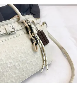 Detail of cream crossbody bag featuring geometric texture and chocolate-shaped charm decoration