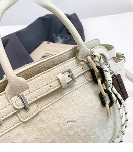 Detail of cream lychee leather handbag featuring decorative buckle and creative charms
