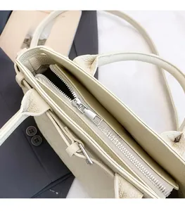 Detailed top view of a cream leather tote bag featuring a silver zipper and sturdy handles