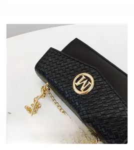 Detail of black woven texture leather bag with gold circular logo and chain strap
