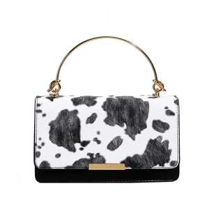 Chic cow print handbag with gold ring handle and metal clasp in a stylish square shape