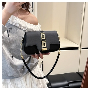 Close-up of minimalist black leather saddle bag with golden Greek key metal buckles