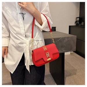 Detail of red saddle bag featuring a gold buckle with Greek key pattern and chain strap