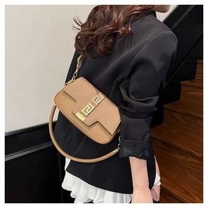 Detail of a brown leather saddle bag featuring a gold Greek key buckle and lychee texture