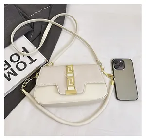 Detail view of cream saddle bag showing geometric gold buckle and size relative to a phone