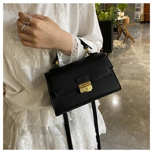Close-up of black lychee grain texture and gold metal clasp on a minimalist handbag