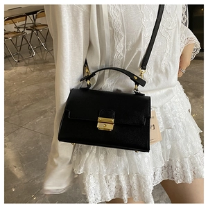 Detail of black lychee texture crossbody bag with gold metal clasp and top handle
