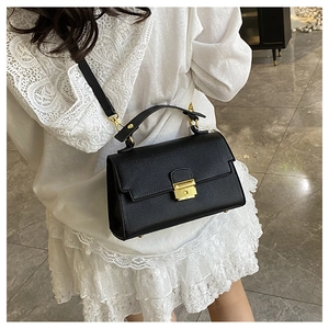Detail of elegant black textured crossbody bag with gold buckle and top handle strap