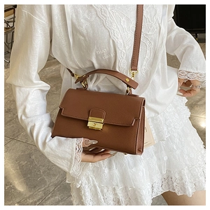Detailed view of brown lychee-grain leather handbag with golden metal twist lock and strap