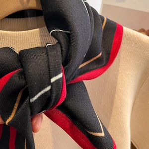Détail d'un foulard en soie tricolore rouge et noir avec texture sergé sur un pull beige