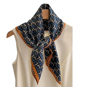 Carré de soie aux motifs géométriques bleus et bordure caramel sur un cintre