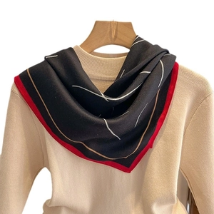 Élégant foulard en soie noir avec lignes dorées et bordure rouge sur un pull beige