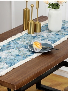 Close-up of vintage floral table runner with dense white tassels on a wooden dining table