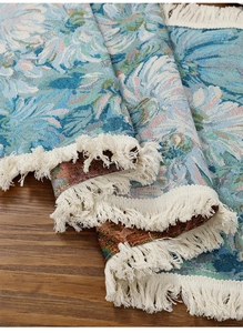 Detail of vintage blue floral jacquard runner with white tassel fringe on wood
