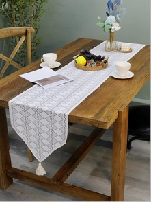 Detail of white table runner with grey geometric triangles and white tassel on wood table