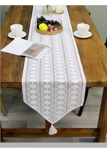 Detailed texture of white lace table runner with geometric patterns and fringe tassel