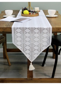Close-up of white lace table runner with hollow geometric patterns and tassel detail