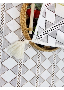 Close-up of white lace table runner with geometric diamond patterns and tassel details