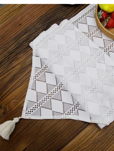 Close-up of white lace table runner with geometric diamond patterns and tassel edge