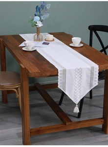 Detail of white lace table runner with geometric embroidery and tassel on wood table