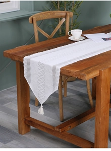 Close-up of white lace table runner with geometric hollow patterns and fringe tassels