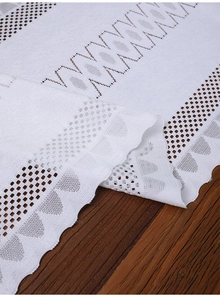 Close-up of white lace table runner with hollow geometric mesh and wavy floral edges