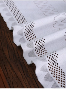 Close-up of white lace table runner with hollow geometric patterns and scalloped edges