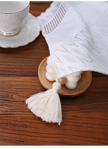 Detail of white lace table runner featuring hollow embroidery and long tassel on wood