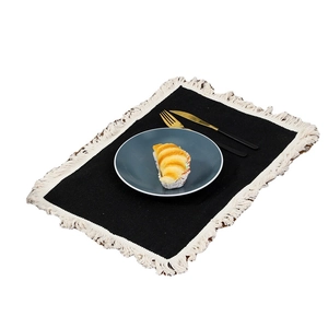Rectangular black linen placemat with cream fringes, featuring a ceramic plate and cutlery