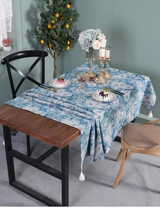 Detailed close-up of blue floral table runner with white fringe tassels on wooden table