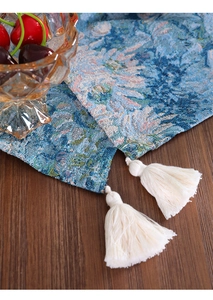 Close-up of blue floral jacquard table runner with white decorative tassels on wood