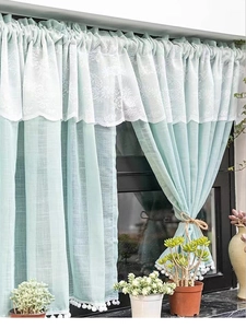 Detail of light green curtains with floral lace trim and white pom-pom edges in a room