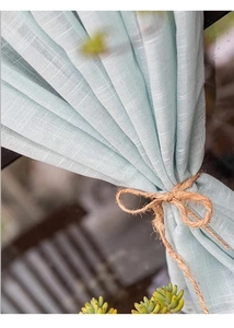 Detail of mint green linen curtain with natural texture and rustic twine tie-back