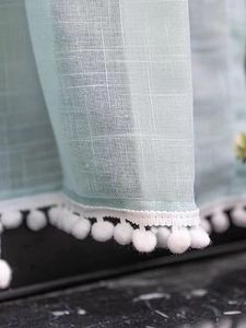 Detail of light blue sheer curtain featuring white pom-pom lace trim and mesh fabric