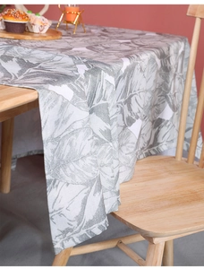 Detail of white linen tablecloth with grey leaf patterns draped on a wooden table