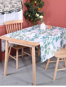 Detail of linen tablecloth with green monstera plant prints on a wooden table