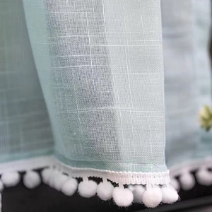 Mint green linen curtain with white pom-pom trim detail in soft natural light