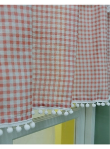 Detail of orange plaid cafe curtain featuring white pom-pom trim and linen texture